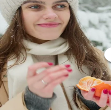 Young woman enjoying a peeled orange in snowy outdoors.