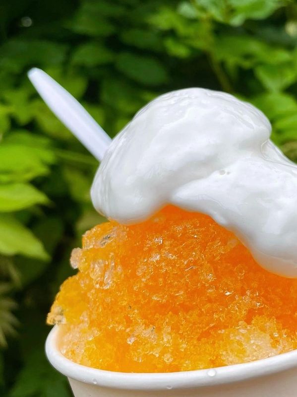 Close-up of an orange shaved ice topped with white cream.