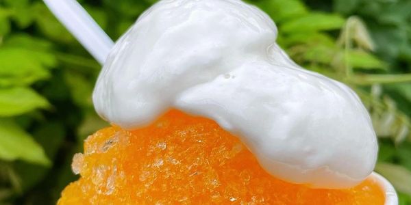 Close-up of an orange shaved ice topped with white cream.