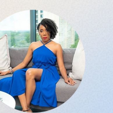 Woman in a blue dress sitting confidently on a couch.