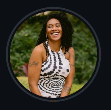 Smiling woman in a black and white tie-dye dress outdoors.