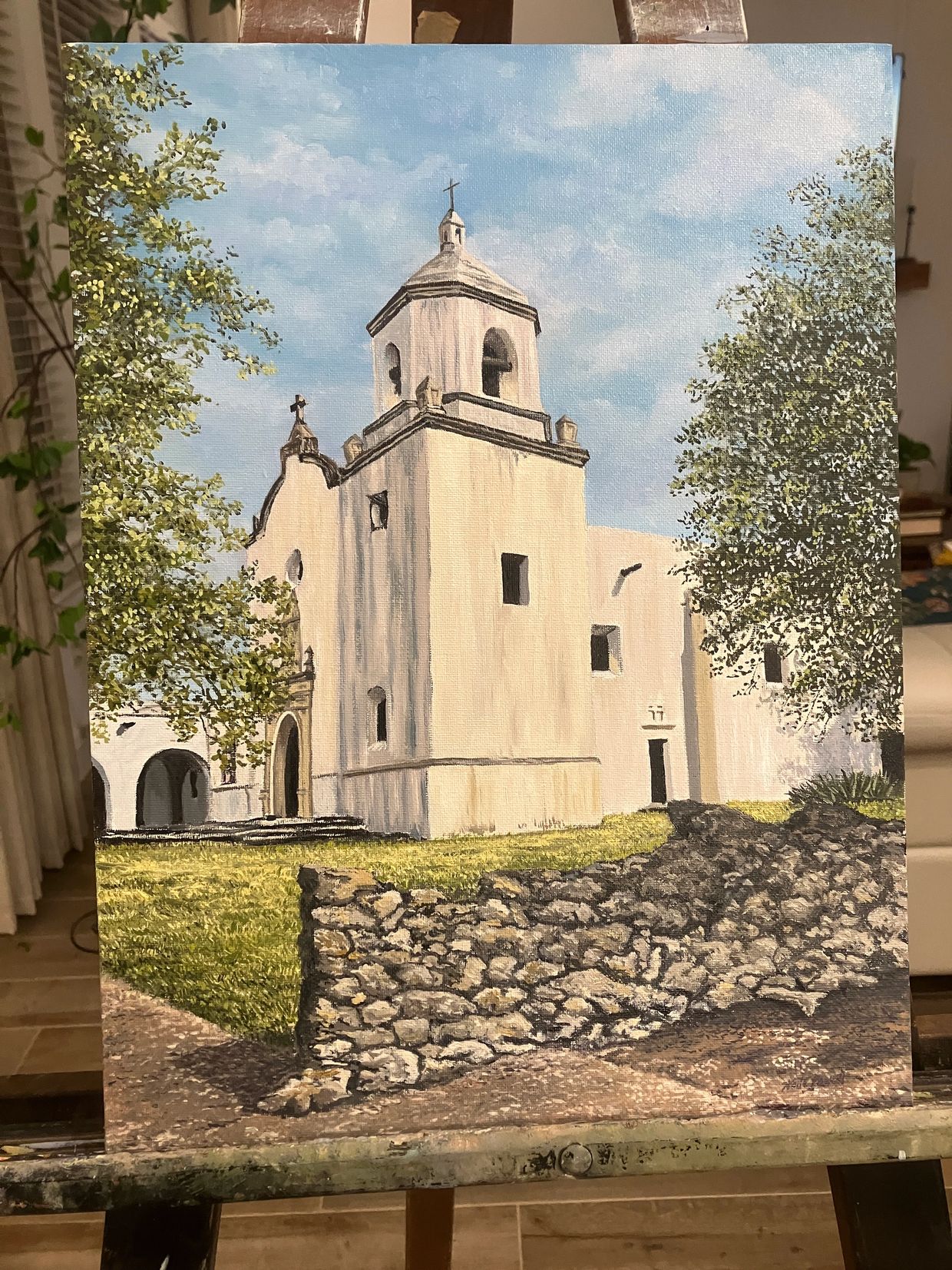 Painting of a historic white church with trees and stone wall under a blue sky.