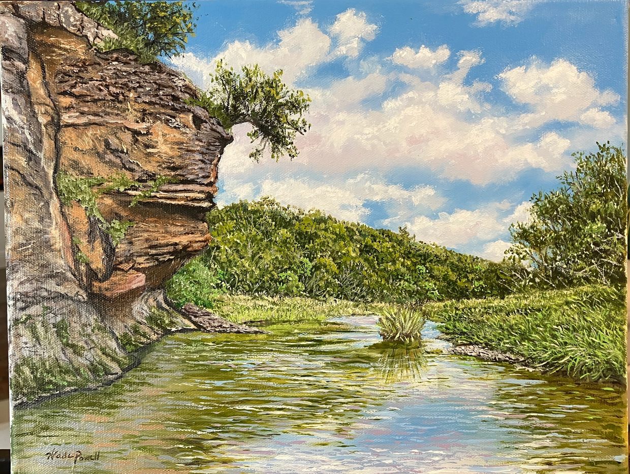 A serene river flows beside rocky cliffs and lush greenery under a blue sky.