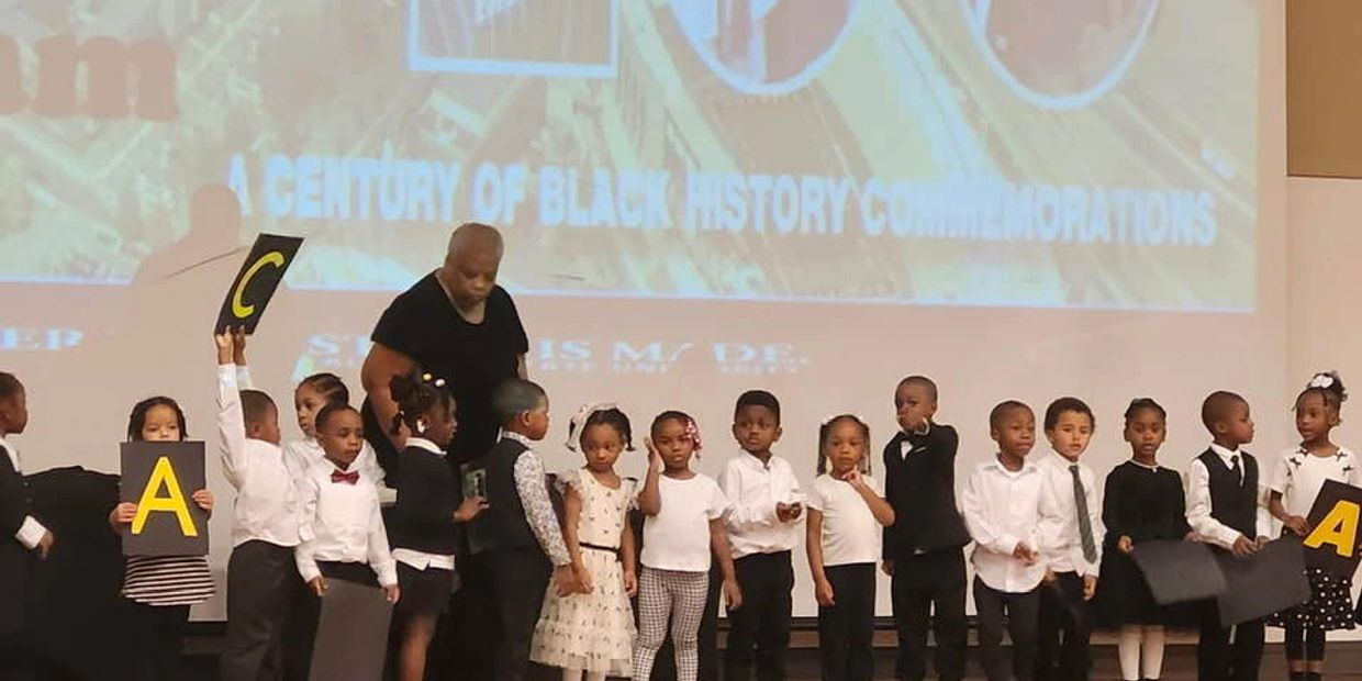 Children on stage holding letters during a Black History Month event.