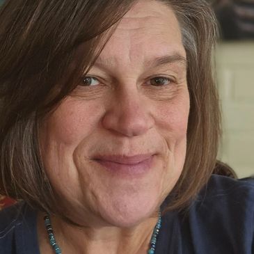 Close-up of a smiling woman with short brown hair and a beaded necklace.