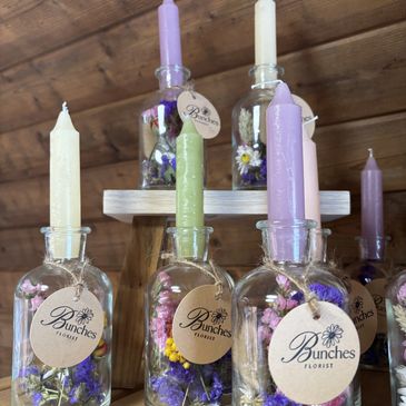 Glass bottles with pastel candles and dried flowers on display.