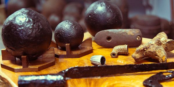 Various antique cannonballs and metal artifacts displayed on a wooden surface.