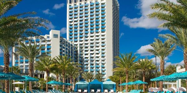 Tall hotel building with blue balconies and palm trees under a clear sky.