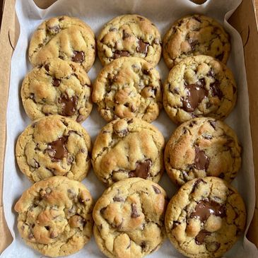 A box of freshly baked chocolate chip cookies with melted chocolate.