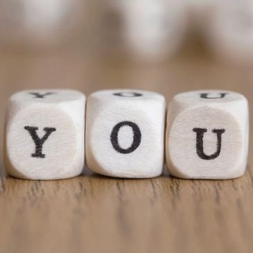 Wooden blocks spelling the word 'YOU' on a wooden surface.