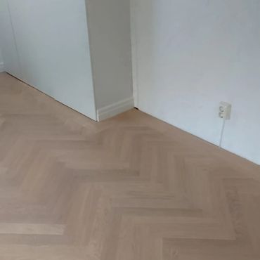 Light wooden herringbone floor with white walls and doors.