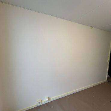 Empty beige wall with electrical outlets and protective floor covering.