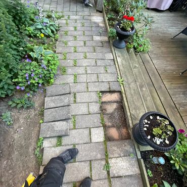 Person repairing a garden path with paving stones and plants around.