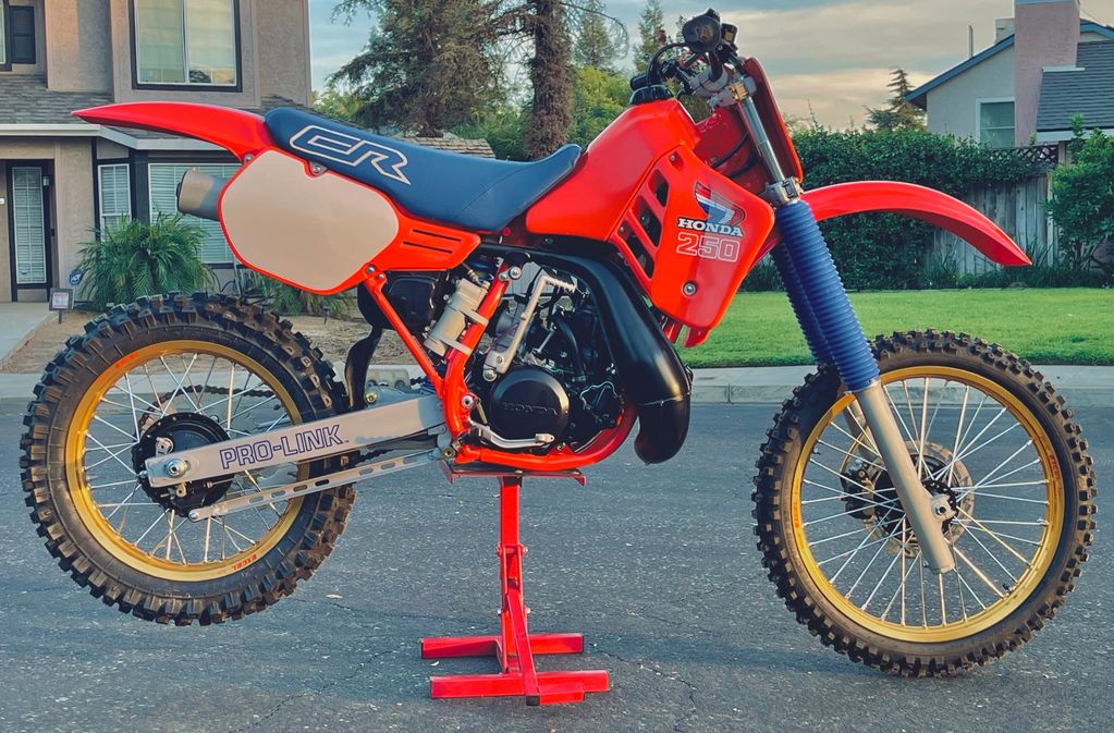 A red Honda CR 250 dirt bike on a stand outdoors.
