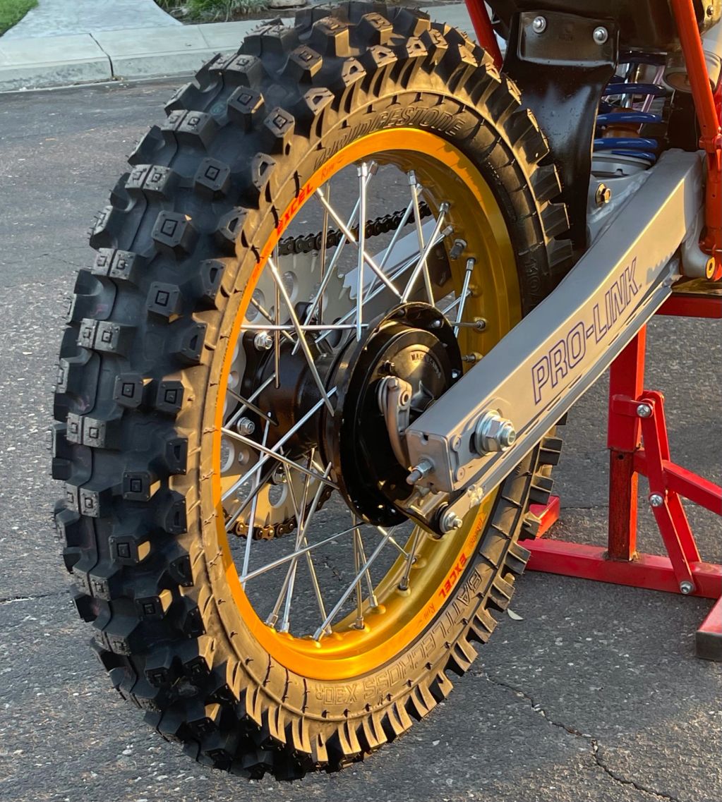 Close-up of a dirt bike rear wheel with knobby tire and gold rim.