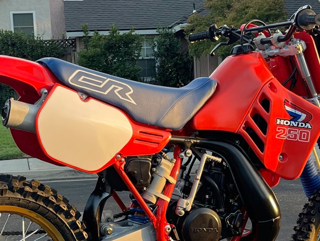 Close-up of a red Honda CR 250 dirt bike with a blue seat and knobby tires.