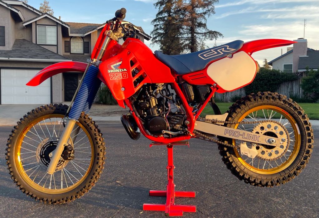 Vintage red Honda CR 250 dirt bike on a stand outdoors.