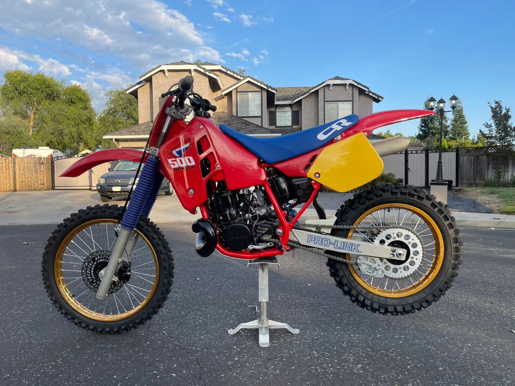 Vintage red Honda dirt bike with gold rims on a stand.