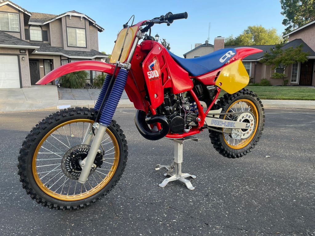 A red Honda CR 500 motocross bike with knobby tires and blue seat.