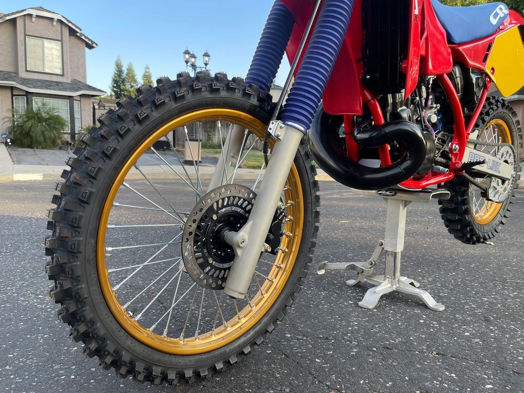 Close-up of a dirt bike tire with gold rim and blue suspension.
