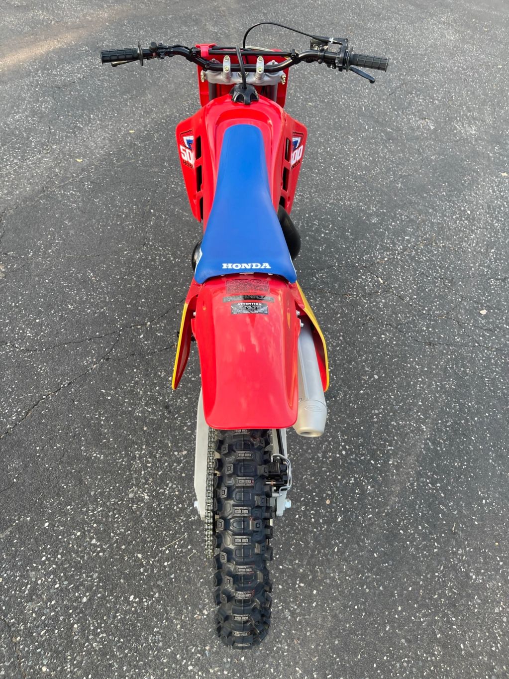 Red Honda dirt bike with blue seat on asphalt.