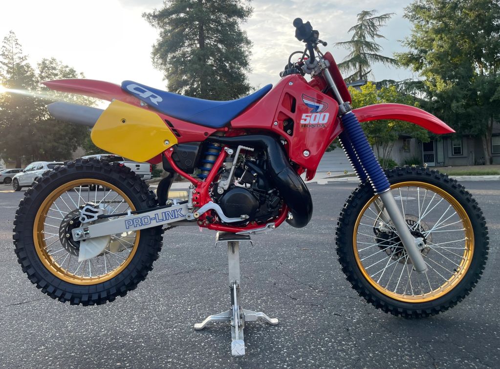 Classic red Honda CR 500 dirt bike with blue seat and gold rims on a stand.