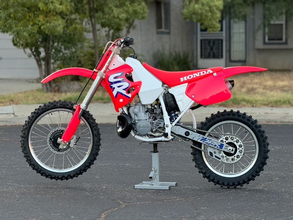 Red and white Honda dirt bike on a stand outdoors.