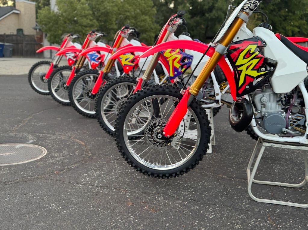 A row of red dirt bikes lined up on pavement with trees in the background.