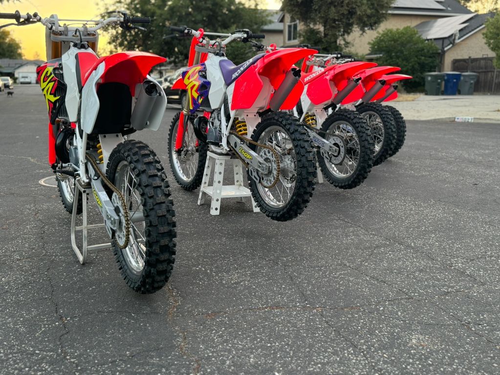 A row of five red and white dirt bikes parked on the street.