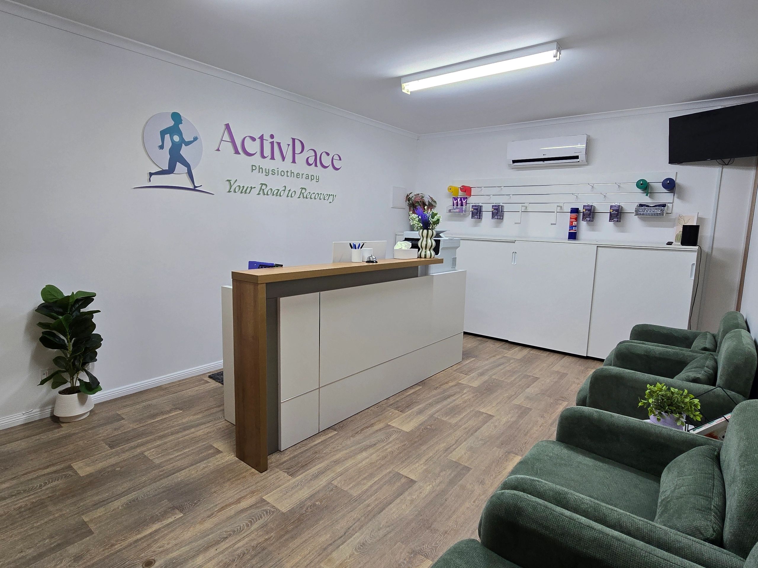 Modern physiotherapy reception with green chairs and wooden flooring.