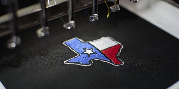Embroidery machine stitching Texas flag design on black fabric.