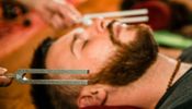 A man with a beard receiving a tuning fork therapy.