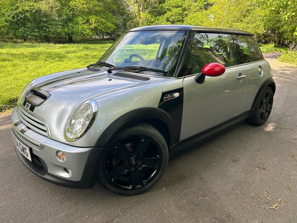 Silver Mini Cooper S with black wheels and red side mirrors parked on a road.