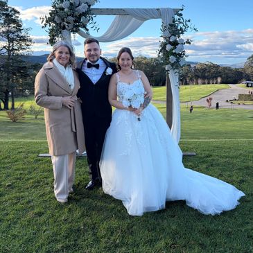 Newlyweds and guest posing outdoors by floral arch