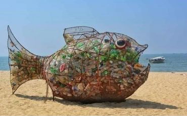 A fish shaped recycling collection point on a beach.