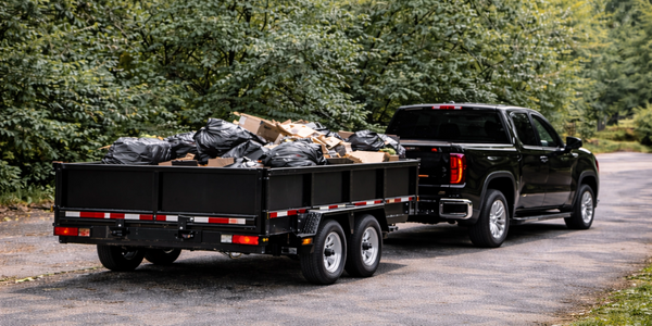 Black pickup truck towing a trailer loaded with garbage bags and cardboard.