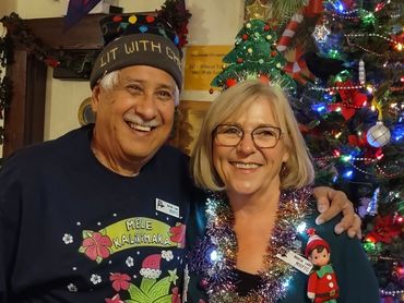 Two smiling people celebrating Christmas by a decorated tree.