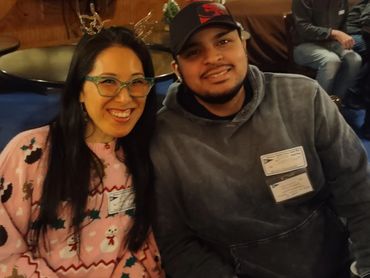 Two people smiling, one wearing a festive sweater and the other a cap.
