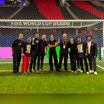Group photo of nine people in a soccer stadium.
