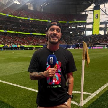 Man with microphone at a sports stadium corner flag.