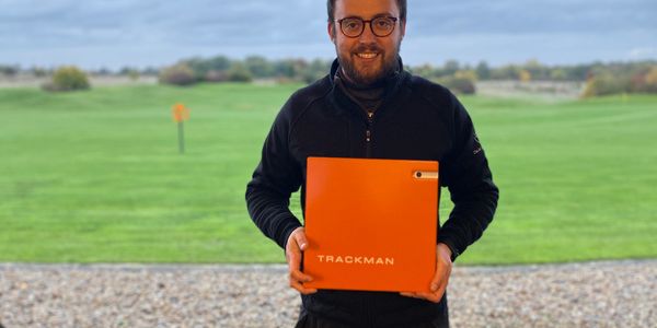 David Laffar holding a trackman radar unit standing on a golf driving range 