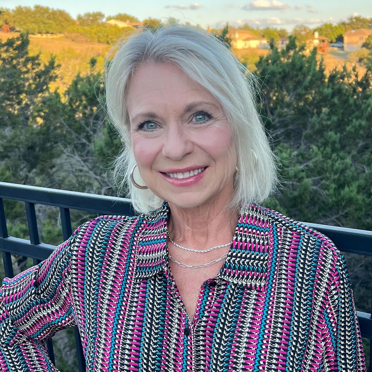 Smiling woman with short blonde hair in a colorful patterned shirt outdoors.