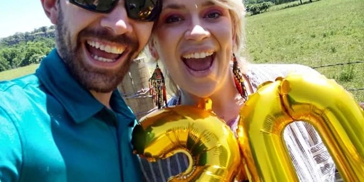A joyful couple holding golden balloons shaped as numbers 2 and 0 outdoors.