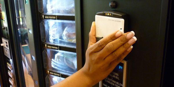 A hand holding a card to a vending machine's card reader.