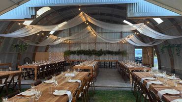 Soft draping and warm festoon lights suspended across a barn ceiling, creating a romantic canopy.