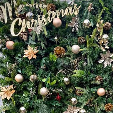 Dense greenery backdrop styled with gold ornaments, pinecones, and subtle decorative accents.