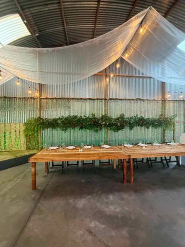 Sheer white draping overhead with warm festoon lighting, paired with a dense greenery garland.