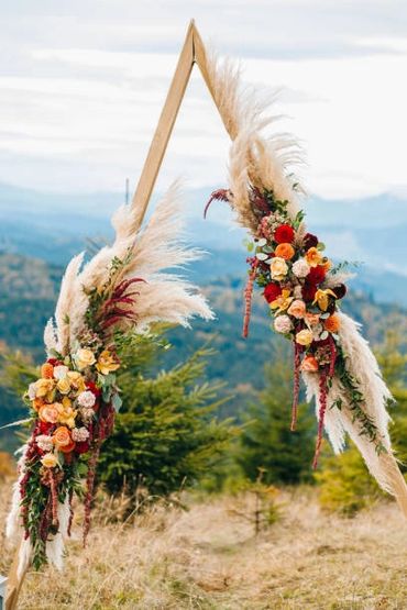 Pampas grass and colourful roses on simple wooden triangular wedding arch for outdoor wedding.