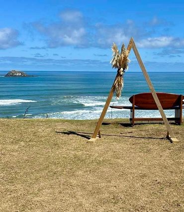 Wooden arch with dried foliage accents, styled as a natural coastal backdrop for beach wedding.