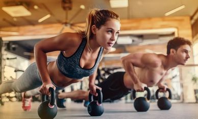 Man and woman doing push-ups on kettlebells.